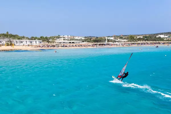 Luftaufnahme zeigt einen Windsurfer auf dem hellblauen Meer, vor dem Santa Maria Strand von Paros, Griechenland
