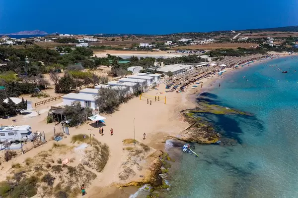 Luftbild des belebten Urlaubsorts und Strand Santa Maria auf Paros, Griechenland, mit Beachvolleyballfeld und Sonnenliegen