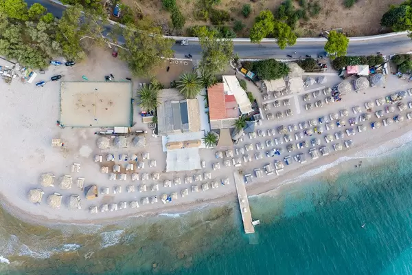 Luftbild des griechischen Καiκι-Strands, mit Bastsonnenschirmen und Touristen auf Strandliegen, an der Küste von Spetses