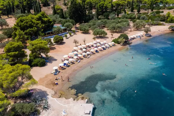 Luftbild des weißen Sandstrands mit Sonnenschirmen und Strandliegen, vor der Zogeria Strandbar auf Spetses, Griechenland