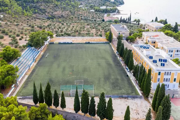 Luftbild eines grünen Fußballfelds mit kleiner Tribüne, am Ligoneri- und Kaikistrand auf der Insel Spetses