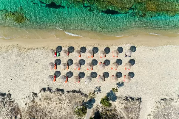 Luftbild: Geometrie am Strand auf Naxos. Drei Reihen von Strandschirmen aus Stroh, Dünen und Meer