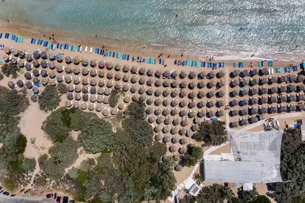Luftbild von aufgereihten Bast-Sonnenschirmen auf dem weißen Sandstrand Santa Maria auf Paros, Griechenland, am türkisfarbenen Mittelmeer