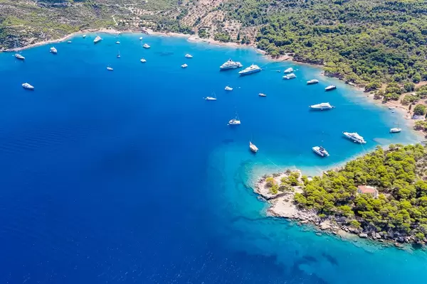 Luftbild von Luxusyachten im blauen Meer am Ekklisia Analipsi Strand auf Spetses und der Agios Georgios Kirche