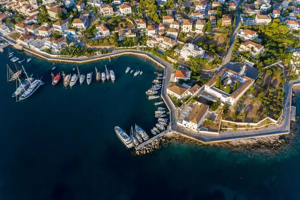 Luftbild von Luxusyachten und Motorbooten an der Küste von Baltiza, Spetses in Griechenland, mit Blick auf die griechische Kirche Agios Nikolaos