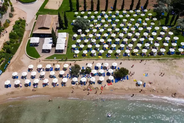 Luftbild von Urlaubern unter aufgereihten, weißen Sonnenschirmen am Strand von Chinitsa, Griechenland