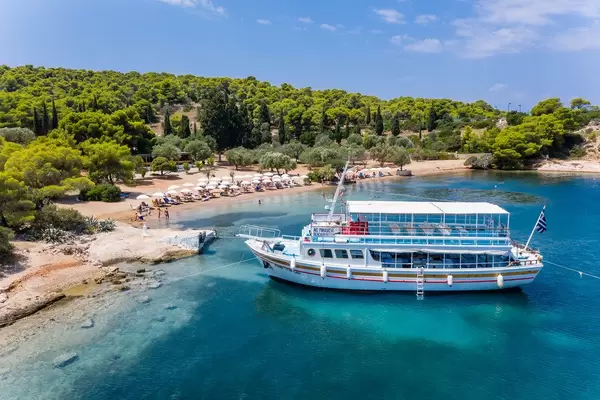 Luftbild zeigt den Ankerplatz der Fähre für Urlauber der Insel Spetses, mit dem grünen Pinienwald hinter dem blauen Argolischen Golf