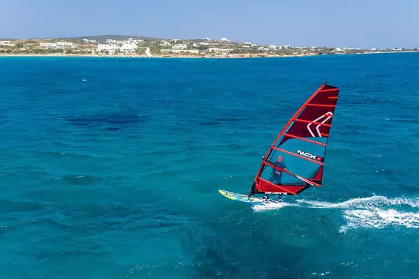 Luftbild zeigt einen Mann beim Windsurfen auf einem Surfbrett mit NCX Segel, der Kurs auf die griechische Insel Paros nimmt
