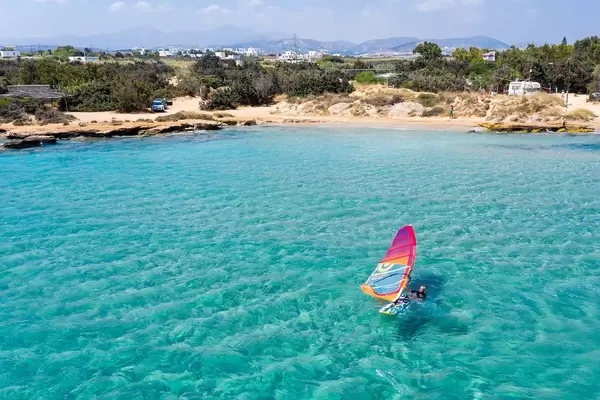 Luftbild zeigt einen Wassersportler beim Windsurfen im türkisfarbenen Mittelmeer, vor dem Santa Maria Strand auf Paros, Griechenland