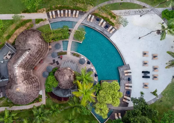 Luftbild zeigt Nahaufnahme des Spabereichs mit blauem, runden Pool, Sonnenliegen und Bast-Sonnenschirm neben Palmen auf Mahé, Seychellen