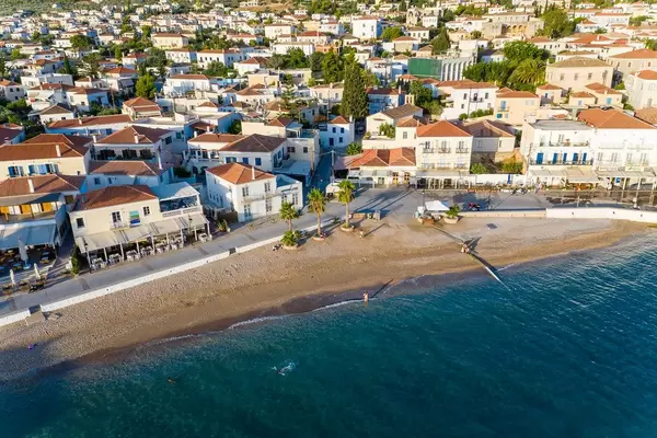 Luftbild zeigt Palmen am Küstenweg des Agios Mamas Strand, mit Häusern im Neoklassizismus-Stil, auf der kleinen Insel Spetses, im Argolischen Golf