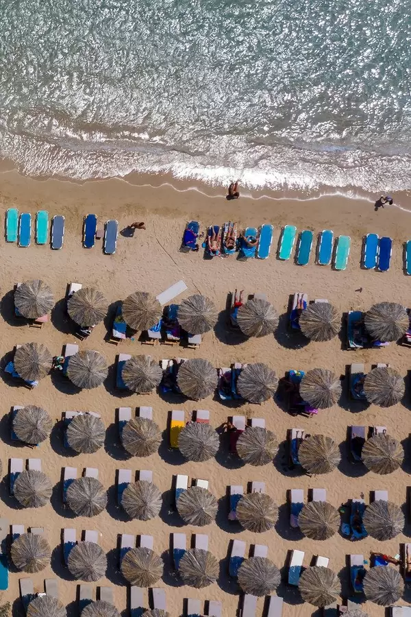 Luftbild zeigt Urlauber auf bunten Sonnenliegen von oben fotografiert und mediterrane Strandschirme