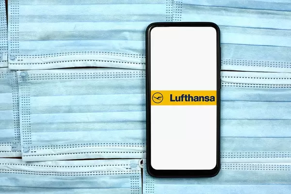 Lufthansa logo on cell phone display over face masks. Impact of coronavirus on global business