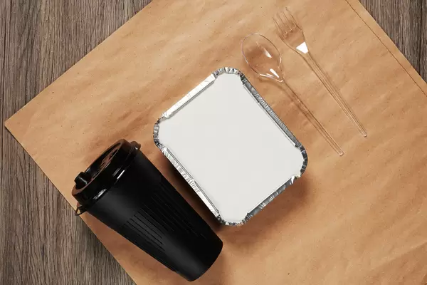 Lunchbox with food, coffee cup, plastic spoon and fork on crafty paper package