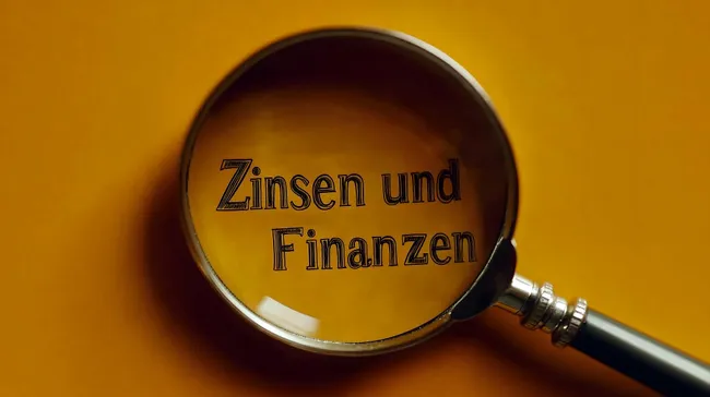 Lupe auf Schriftzug 'Zinsen und Finanzen' auf gelbem Hintergrund