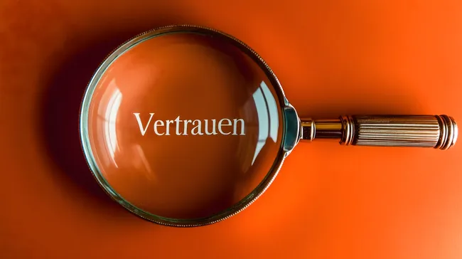 Lupe fokussiert auf das Wort 'Vertrauen' vor orangem Hintergrund
