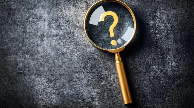 Lupe mit Fragezeichen auf dunkler Oberfläche