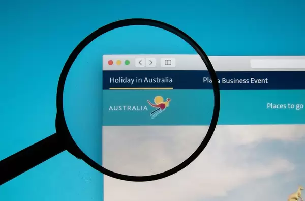Lupe über Bildschirm akzentuiert Logo von Holiday in Australia, der Website für Reisen nach Australien