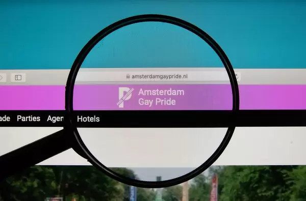 Lupe über Bildschirm betont Logo und Internetadresse der Amsterdam Gay Pride