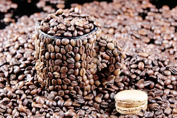 Macaron neben einer Tasse aus Kaffeebohnen mit Kaffeebohnen gefüllt und umgeben