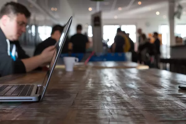 MacBook von der Seite fotografiert und Teilnehmer im Hintergrund