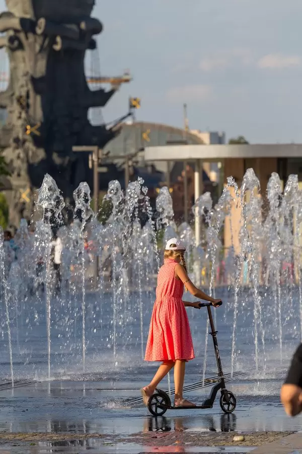 Mädchen fährt mit Roller an einem Springbrunnen vorbei