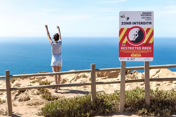 Mädchen hinter dem Geländer der Klippen am Cabo da Roca posiert für ein Foto