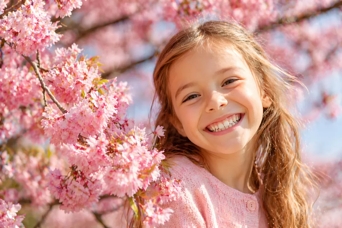 Mädchen lacht strahlend zwischen Kirschblüten im Frühling