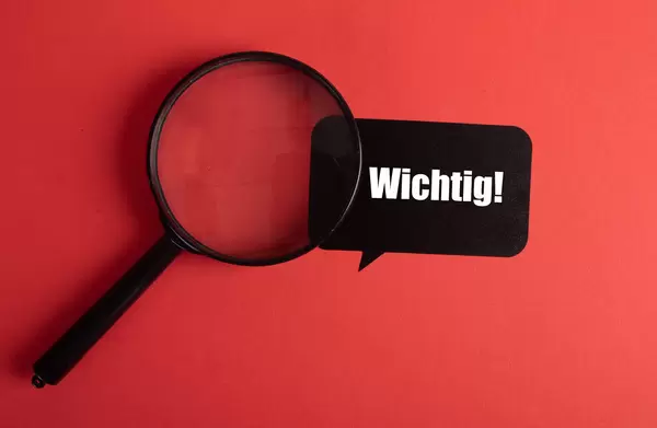 Magnifier and black sticker with Wichtig text on red background