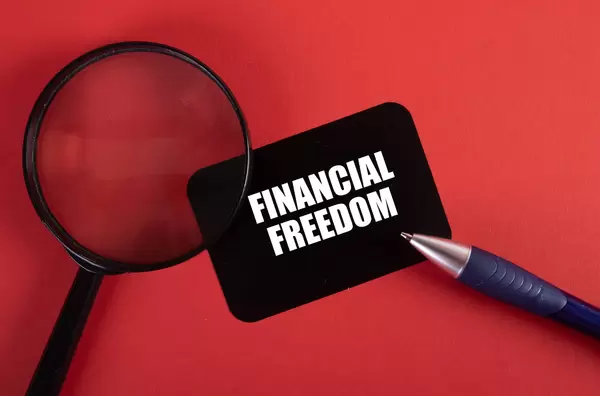 Magnifier, pen and black sticker with Financial Freedom text on red background