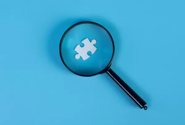 Magnifying glass and puzzle piece on blue background