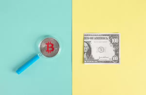 Magnifying glass over sIlver Bitcoin coin and folded dollar banknote