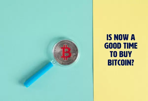 Magnifying glass over sIlver Bitcoin coin and text Is now a good time to buy Bitcoin?