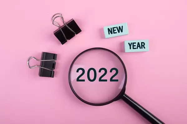 Magnifying glass with paper clips and New Year 2022 text on pink background