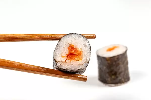 Maki roll with salmon and chopsticks on a white background
