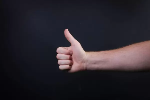 Male hand is showing a thumbs up gesture sign on black background