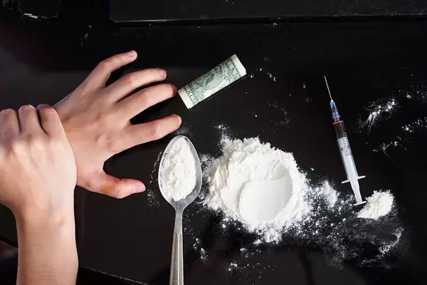 Male junkie hand trying to grab injection syringe of cooked heroine