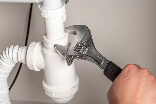 Male plumber fixing sink pipe with adjustable wrench in kitchen