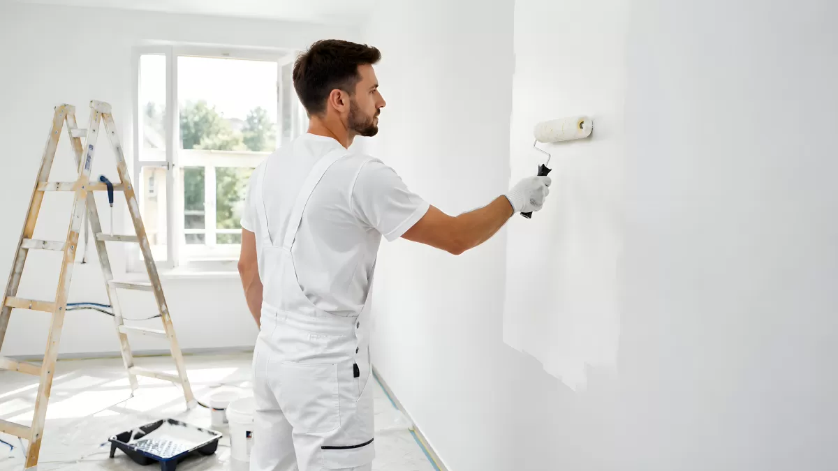 Maler rollt weiße Farbe an Zimmerwand