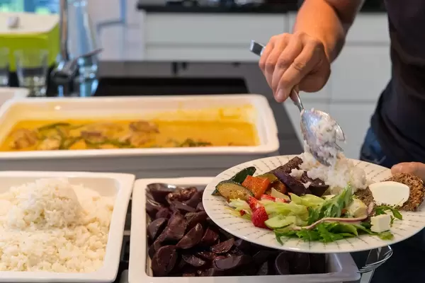 Man at buffet stand scoops white rice on a a healthy dinner plate with salad, vegetables and sliced beetroot
