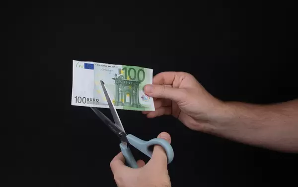 Man cutting 100 Euro banknote with scissors