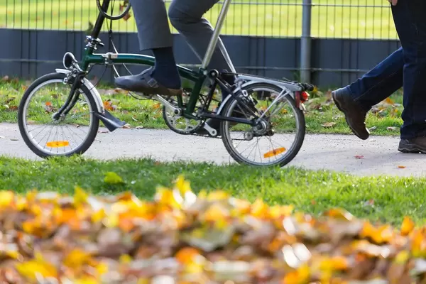 Man cycling in a park with folding bike, sui trousers and house slippers