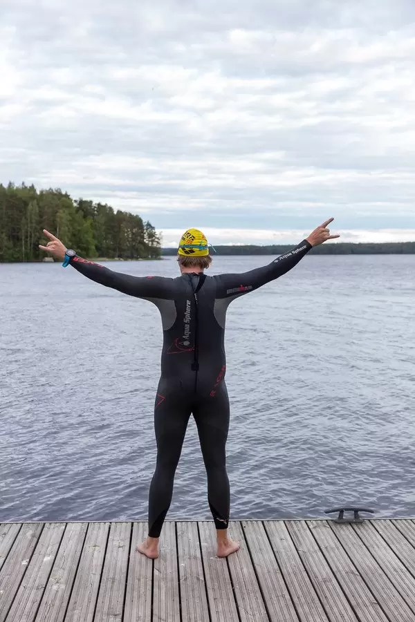 Man from behind with extended arms, in neoprene suit , swimming cap and diving goggles on a wooden jetty at Lake Päijänne in Finland