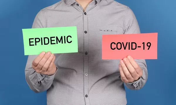 Man holding a green banner with a word epidemic and red banner with Covid-19 text on blue background