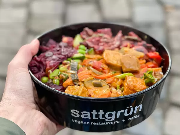 Man holding vegan food to go in the hand: black bowl by vegan restaurant "Sattgrün" in Cologne