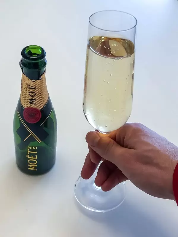 Man holds a glass of champagne next to an empty Mini Moët bottle on a white background