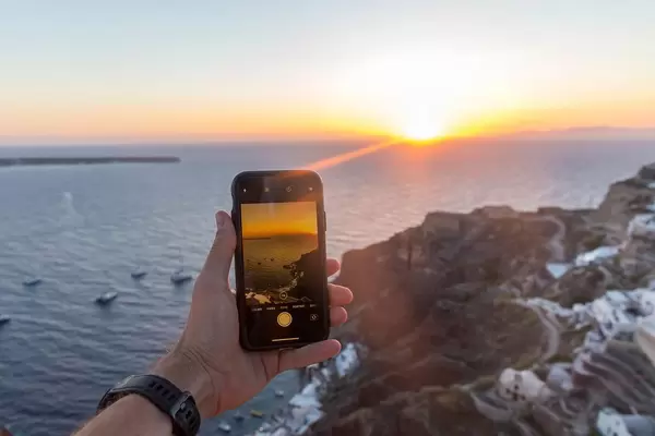Man holds an iPhone in his hand while taking photos of the sunset in Oia, Santorini