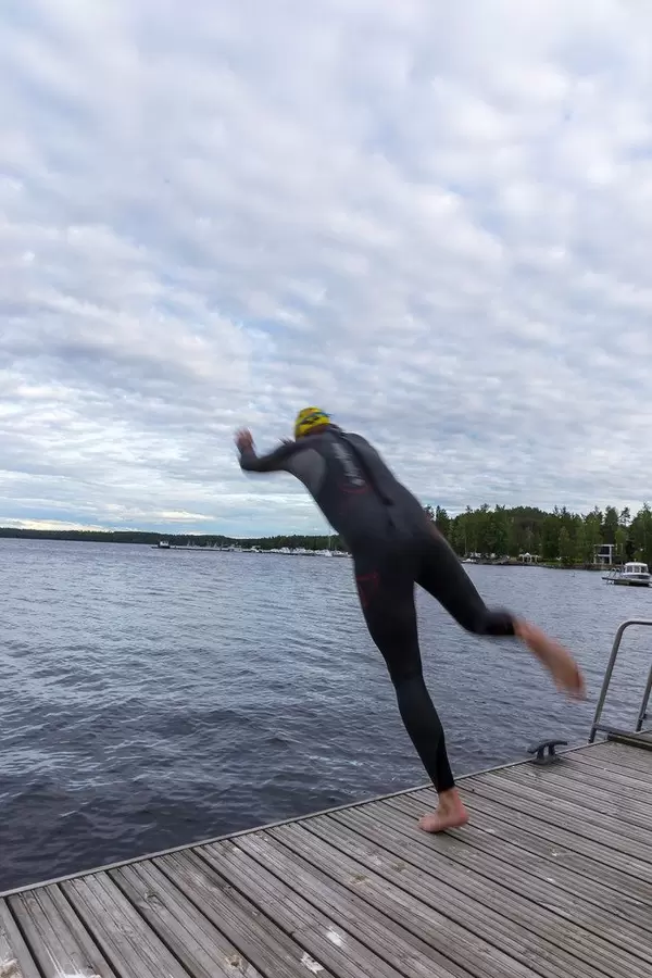Man jumps into a Lake from a wooden walkway, wearing a diving suit, in Padasjoki, Finland
