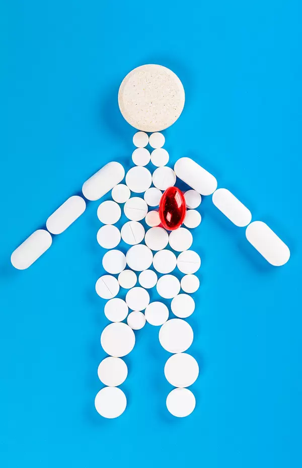 Man made of white pills on a blue background with a red capsule in place of the heart
