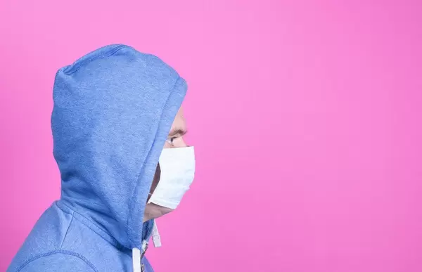 Man mit Kapuzenpulli und Gesichtsmaske auf pinkem Hintergrund